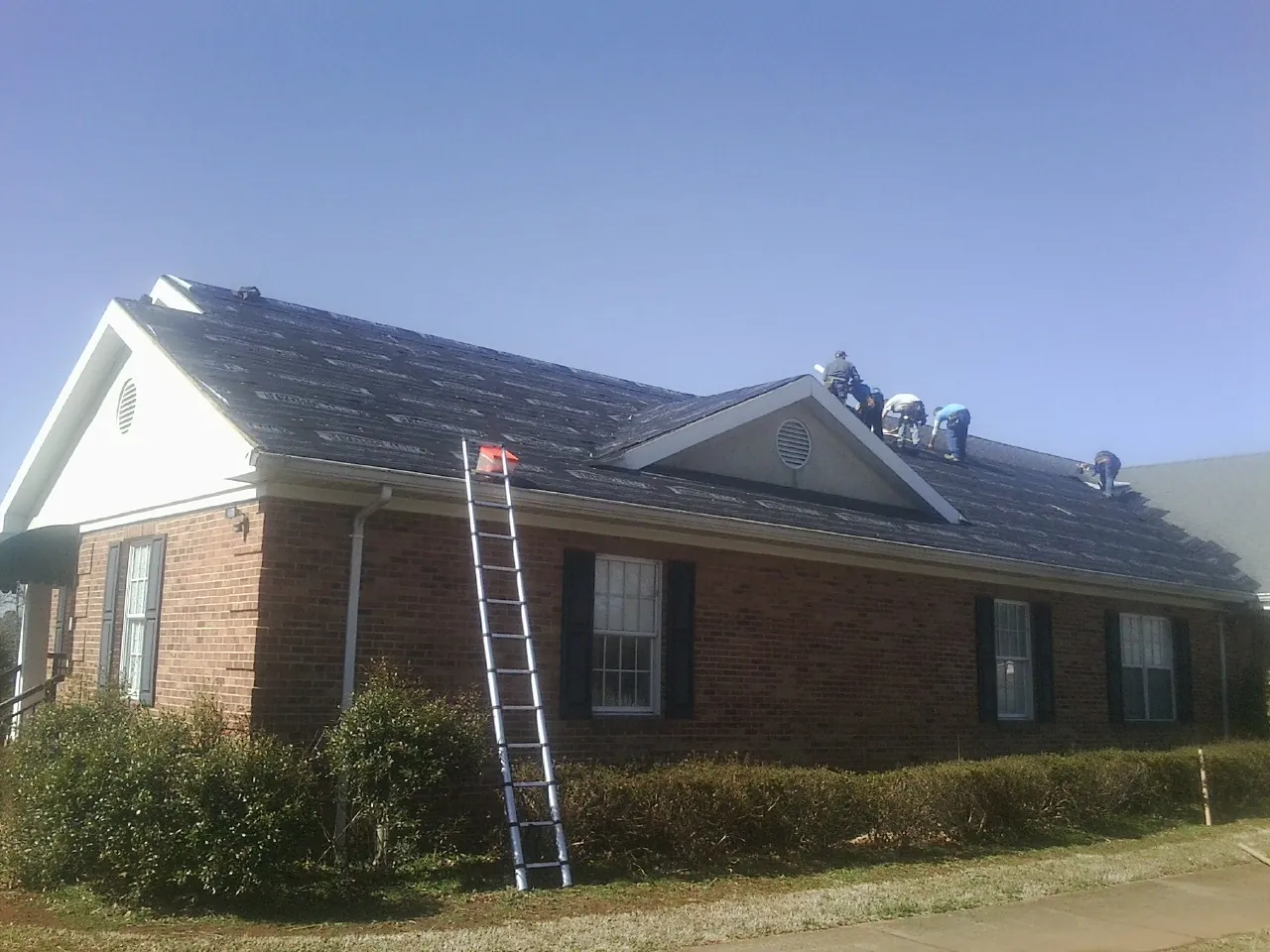 Crew tearing shingles off a brick ranch roof with a ladder set — Metal Roof Repair work by our crew in Cocolamus