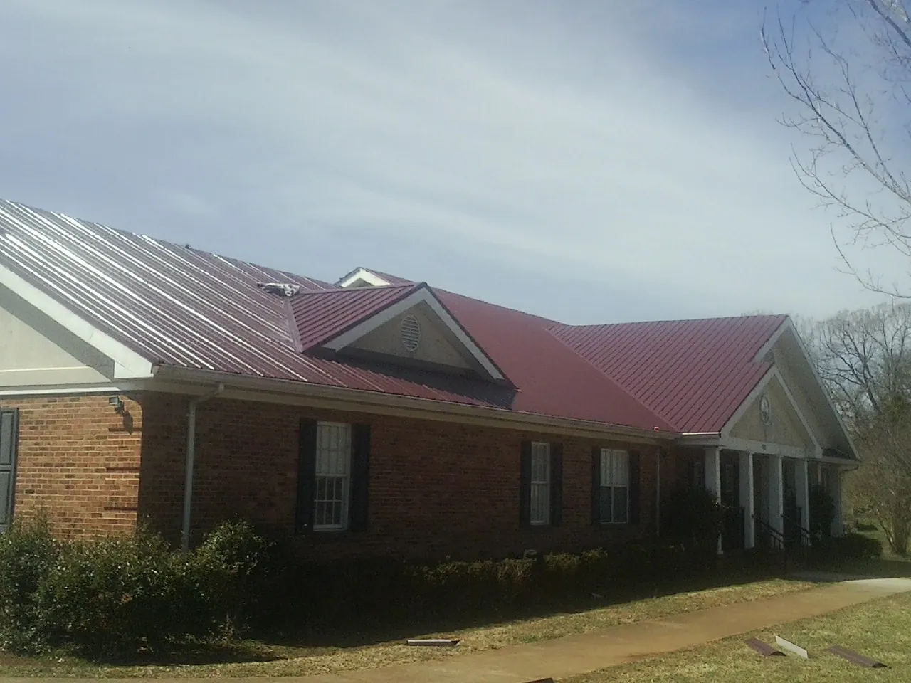 Red metal roof with gabled entries on a long brick building, from a Hail Damage Roof Repair job in Cocolamus