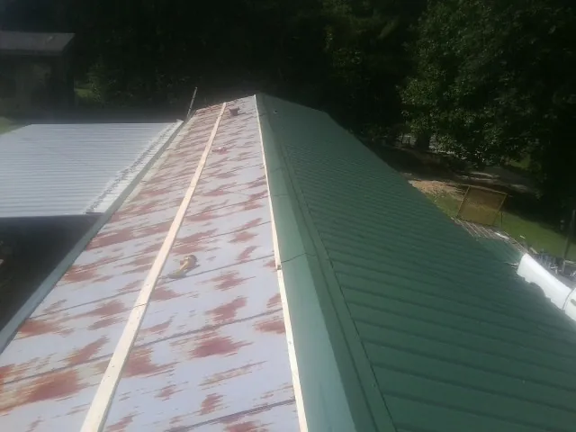 Old rusted panels beside newly installed green metal roofing — Wind Damage Roof Repair by Roofing Brothers in Cocolamus