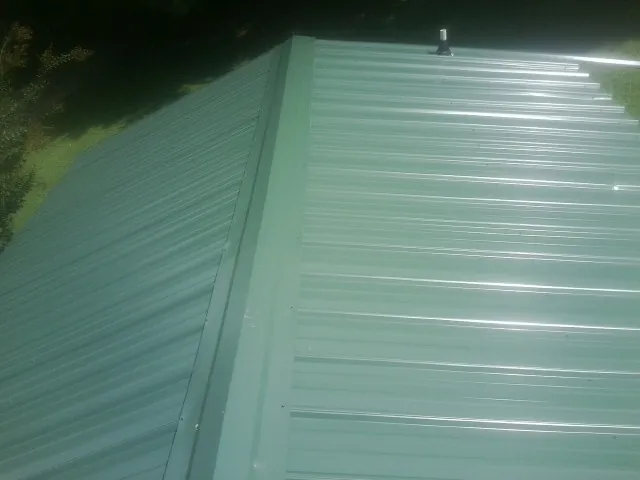 New green metal panels meeting at the ridge of a roof — Flat Roof Repair work by our crew in Cocolamus