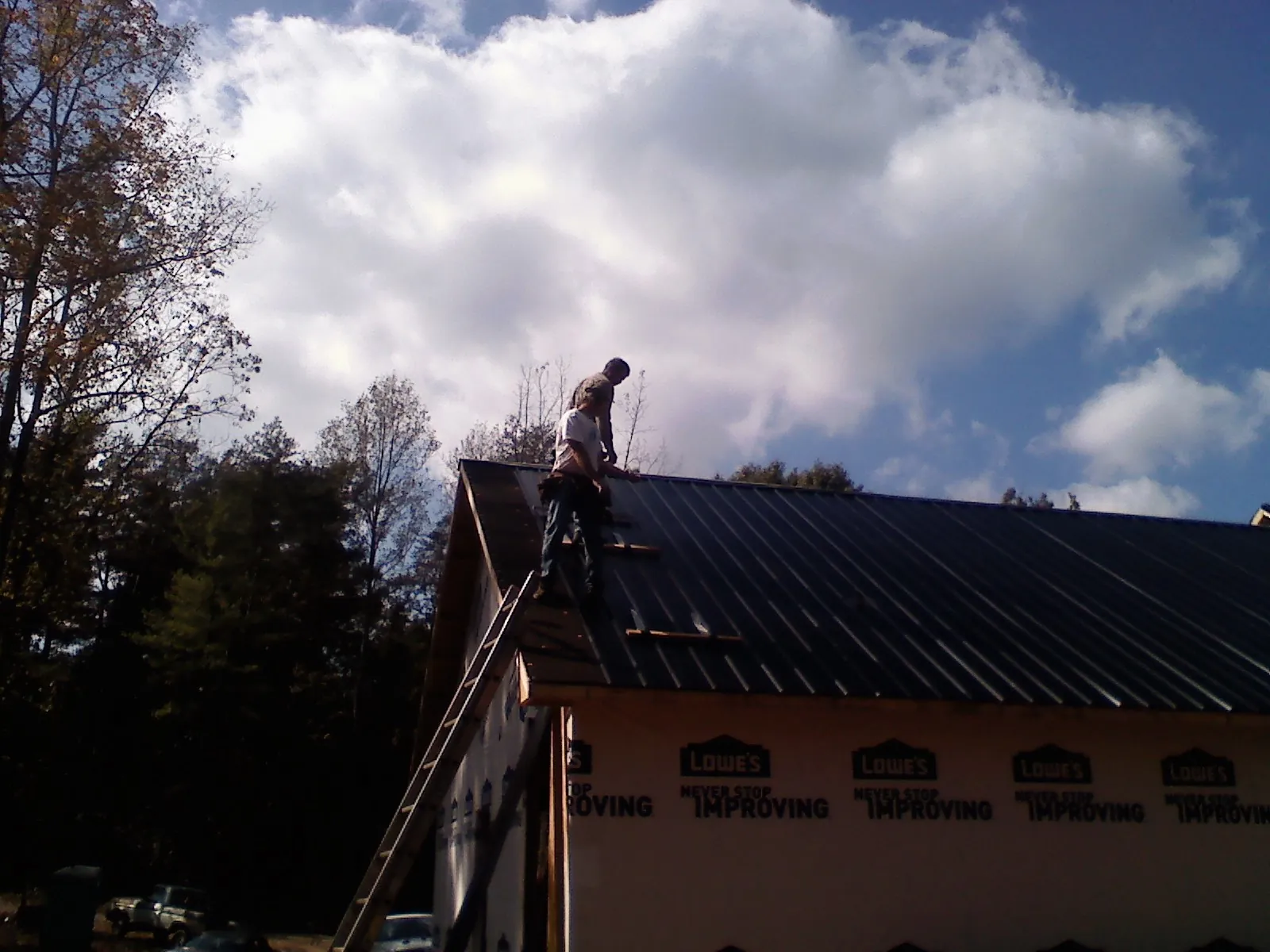 Roofer fastening dark metal panels high against a cloudy sky, from a Roof Inspection job in Cocolamus