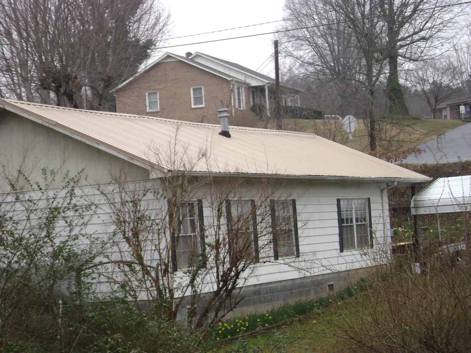 Tan metal roof on a white sided house set into a hillside — Commercial Roofing by Roofing Brothers in Cocolamus